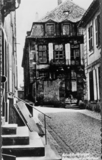 La place du presbytère catholique vers 1930 et, au fond, l'hôtel de ville avant les transformations des années 1950 (disparition du mur de clôture et du portail, ainsi que destruction de la maison de droite).