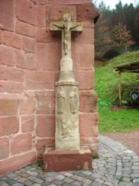 Une croix en grès gris est adossée à la façade de la chapelle.