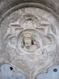 Comme sur une autre croix du cimetière, la pierre tombale est dominée par le visage du Christ couronné d'épines.