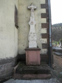Une croix de mission est adossée à la tour-clocher, à gauche de l'entrée de l'église paroissiale.
