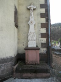 Une croix monumentale est adossée à la tour-clocher de l'église paroissiale, à droite de l'entrée.