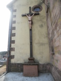 Une croix de mission est érigée à gauche de l'entrée de l'église, contre la façade.