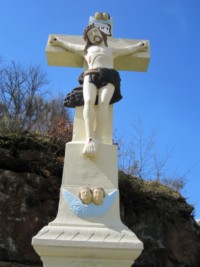 Le croisillon présente, outre le Christ en Croix, deux têtes d'angelots ailées à son sommet : deux autres têtes de ces mêmes angelots sont représentées au sommet du fût-stèle.