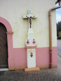 Une croix monumentale est adossée à la façade de la chapelle : elle représente trois cœurs enflammés, qui symbolisent peut-être les trois personnes de la Sainte-Trinité.