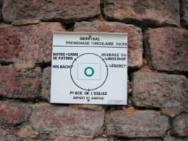 Un panneau du Club vosgien, présentant la promenade circulaire du village et de son patrimoine, est apposé contre le mur entourant l'église Saint-Marc.