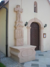 La croix se situe à gauche de l'entrée de la chapelle.