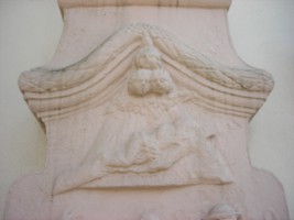 La partie supérieure du fût-stèle représente trois têtes d'angelots ailées, sous lesquelles est représenté le Portement de la Sainte-Croix par un Christ tombant sous le poids.