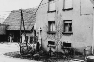 La croix se dresse contre le mur de la maison numéro 67, rue de la colline (photographie du service régional de l'inventaire de Lorraine).