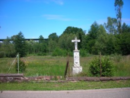 La croix Konrad se dresse dans un jardin, face aux maisons.