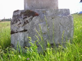 Une sainte femme est représentée sur le socle de la croix : couronnée, il pourrait s'agit de la Sainte Vierge, ou bien plus vraisemblablement de sainte Catherine.