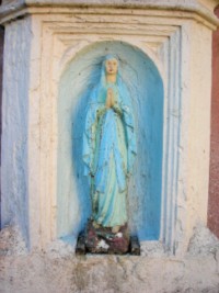 La sculpture en bas-relief de Notre-Dame de Lourdes occupe la niche du fût de la croix.