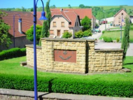 L'arrière du monument aux morts et la place du village, au pied de l'église Saint-Donat et de la mairie-école.