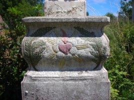 Le socle de la croix est occupé par un cœur enflammé dans une nuée rayonnante.