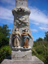 Le fût-stèle galbé représente de bas en haut : la Très Sainte Vierge et saint Jean ; des symboles macabres tels qu'un crâne et des tibias croisés ; trois têtes d'angelots ailées.