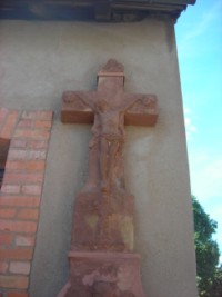 Le croisillon de la croix du hameau d'Eschviller présente deux têtes d'angelots ailées, aux extrémités gauche et droite, surmontées par le buste de Dieu le Père.