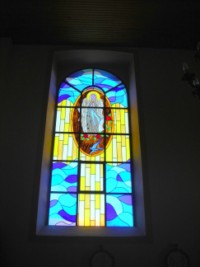 Un vitrail de la chapelle d'Eschviller, à Volmunster, représente l'apparition de la Sainte Vierge à sainte Bernadette dans la cité de Lourdes, en 1858.
