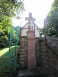 Une croix monumentale est érigée devant la chapelle, au pied des escaliers.